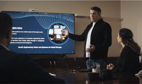 Travis Hohn briefing a team while standing in front of a large TV