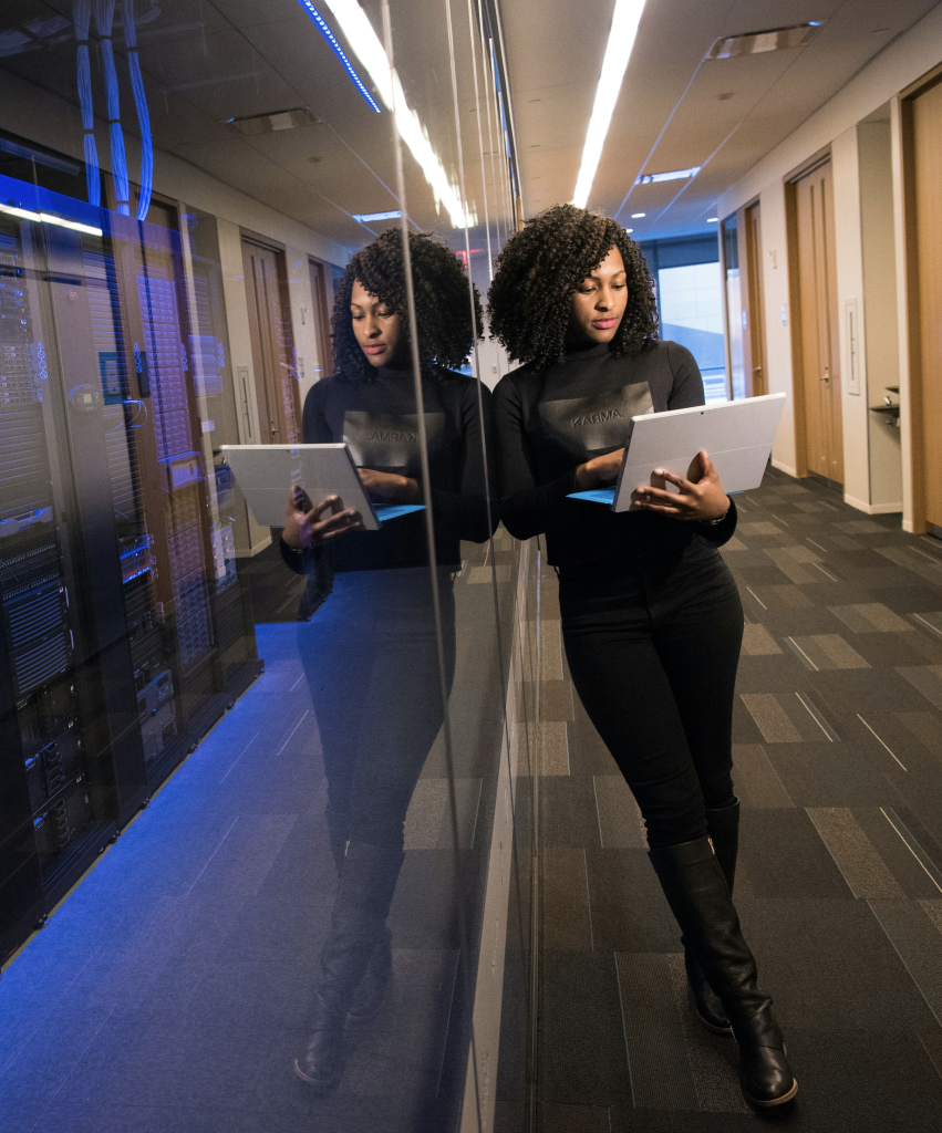 Woman leaning against a glass wall in a data center while working on a computer